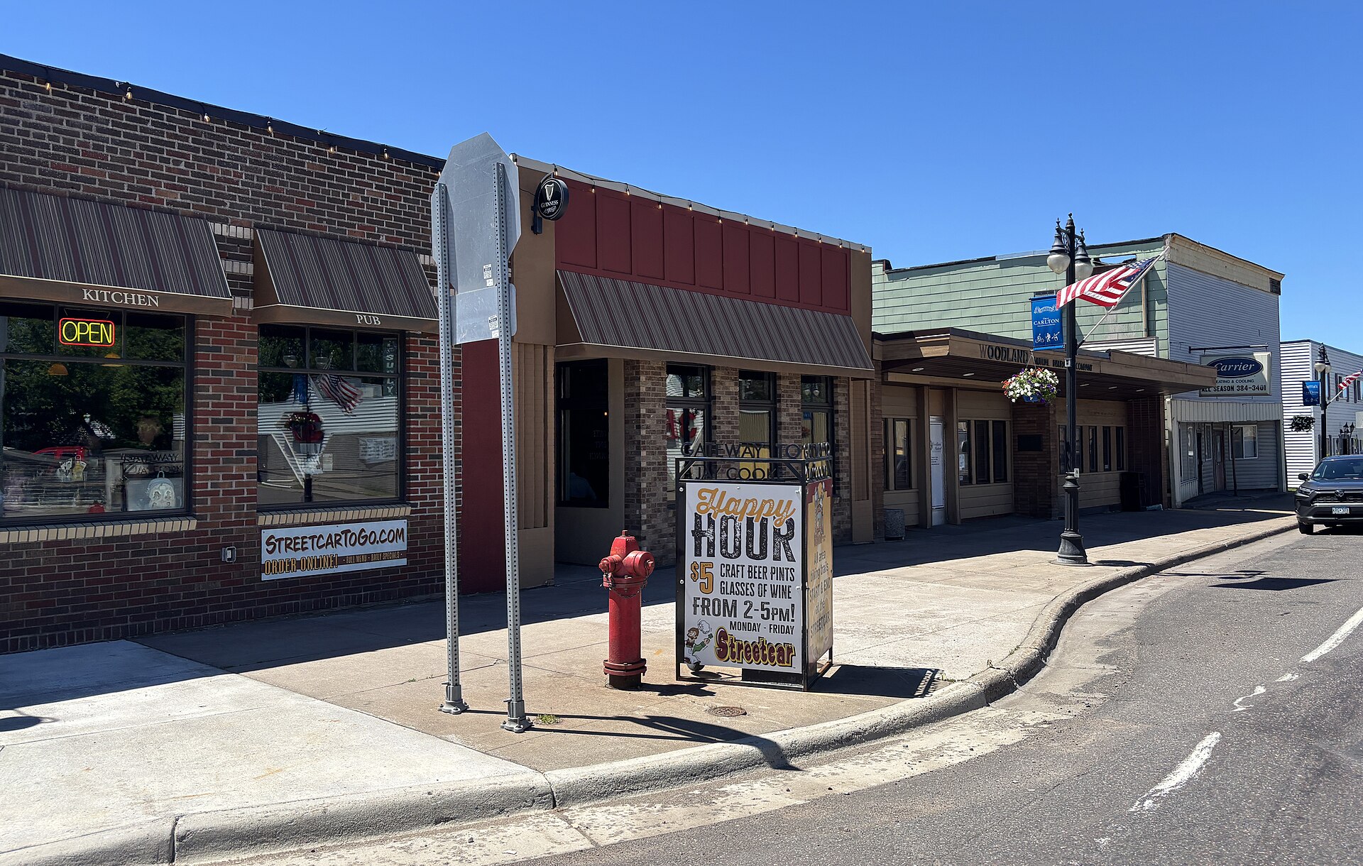 A row of one story brick and clapboard storefronts along Chestnut Avenue in Carlton, Minnesota, with a pub on the corner
