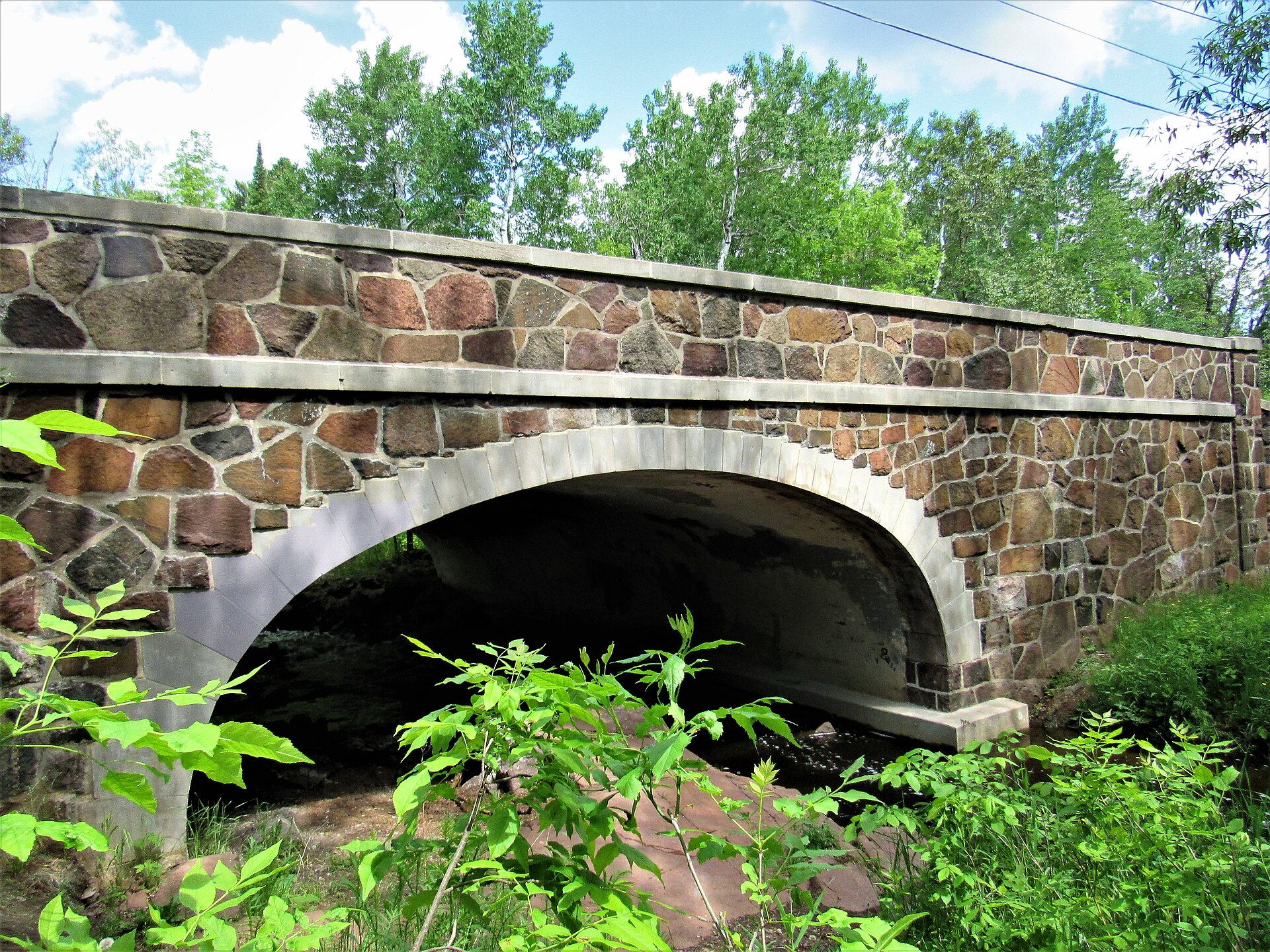 A rustic stone arch bridge carrying a street over Tischer Creek in Congdon Park, Duluth