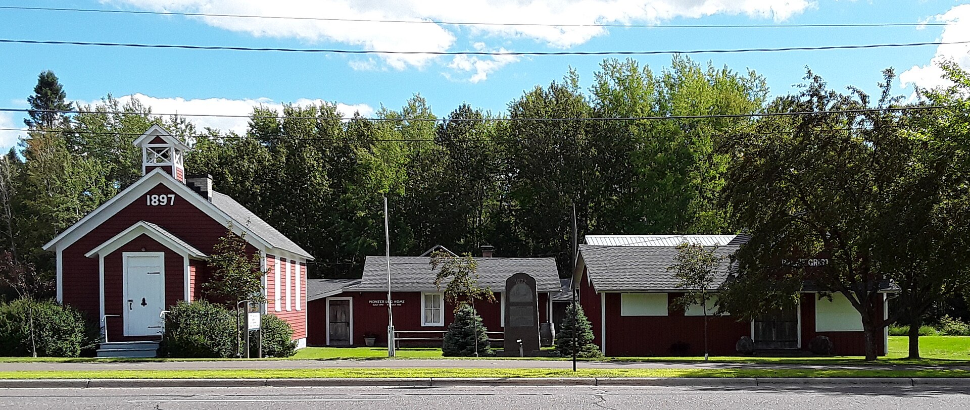 A row of small red buildings including an 1897 one room schoolhouse with a bell tower, set back from the road in Esko, Minnesota