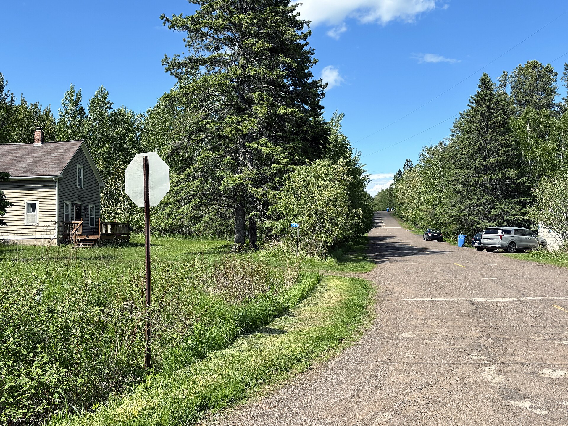 A quiet paved village road in Knife River, Minnesota, with a clapboard house on the left and spruce and birch closing in on both sides