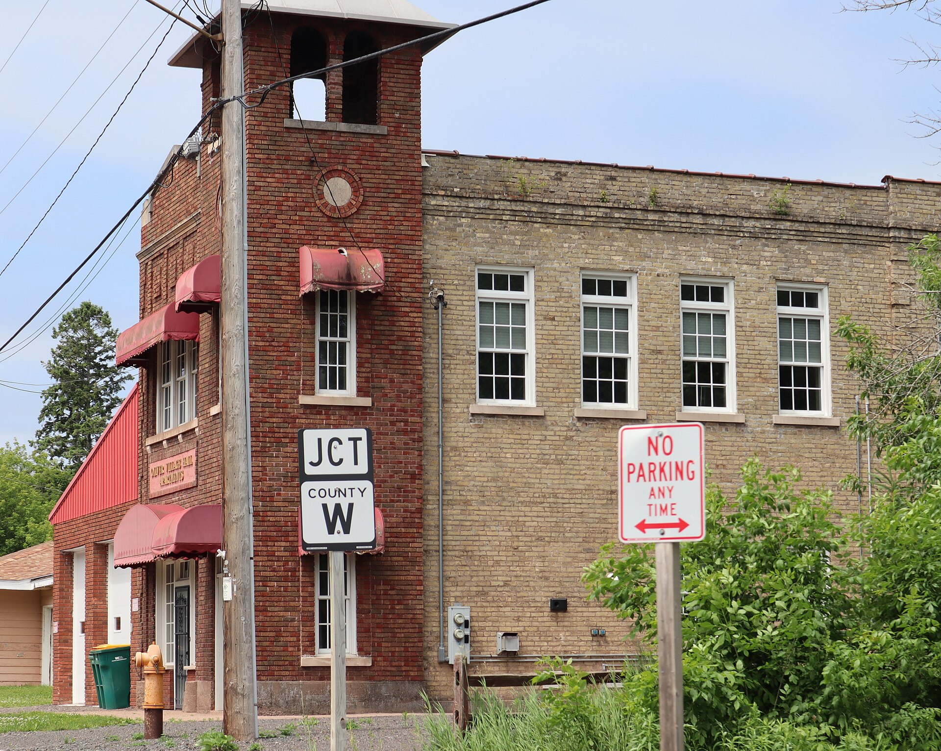 The old village hall in Oliver, Wisconsin, a two tone brick building with a bell tower and red awnings, now apartments