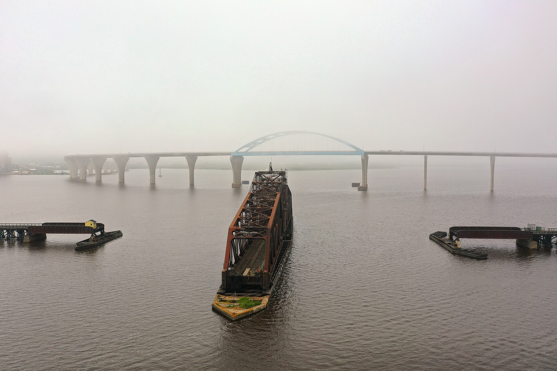 The old Grassy Point swing bridge standing open in the St. Louis Bay on a foggy morning, with the Bong Bridge crossing behind it