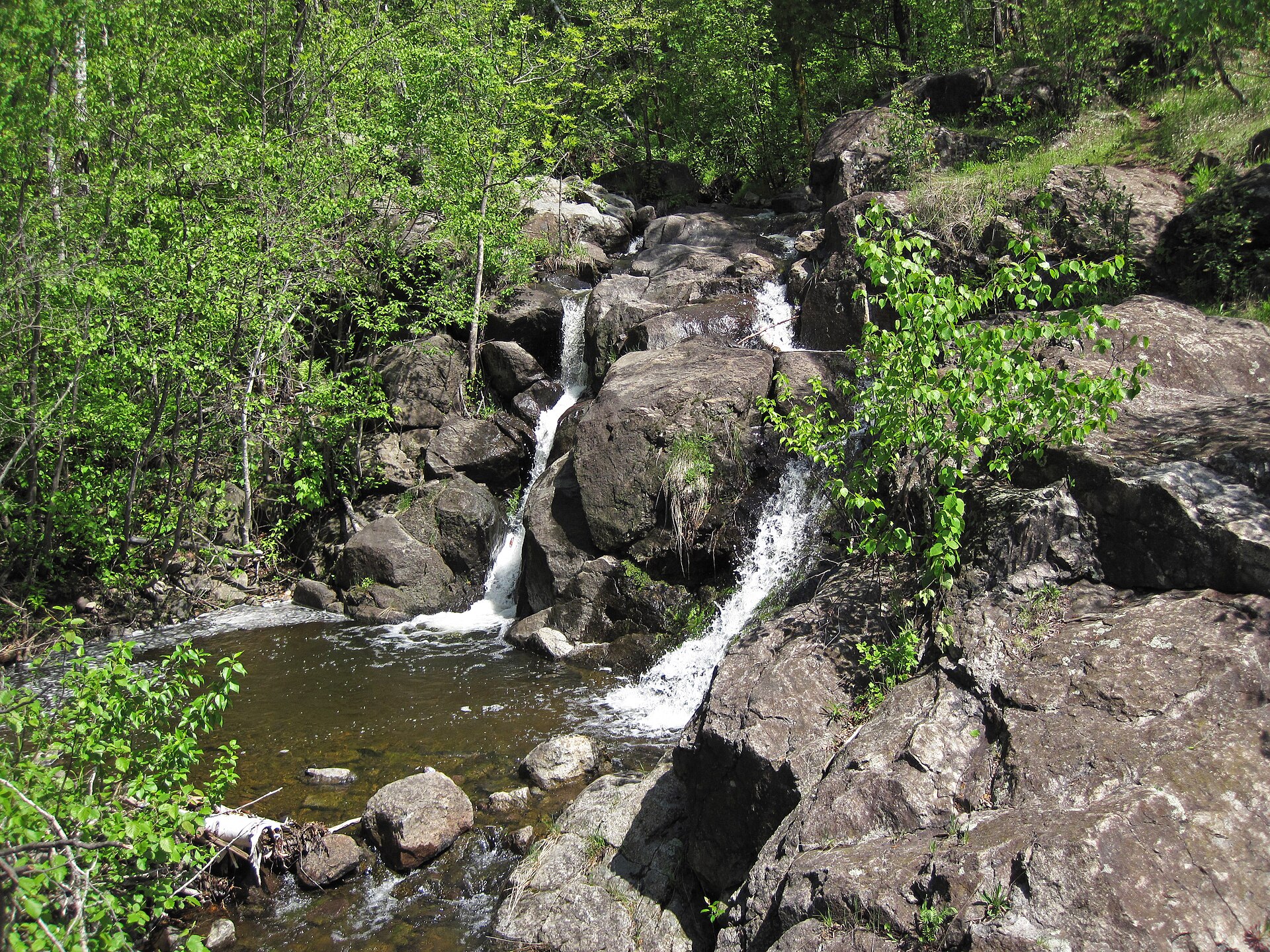 Merritt Creek dropping over dark rock ledges into a pool, in spring woods on the hillside above west Duluth
