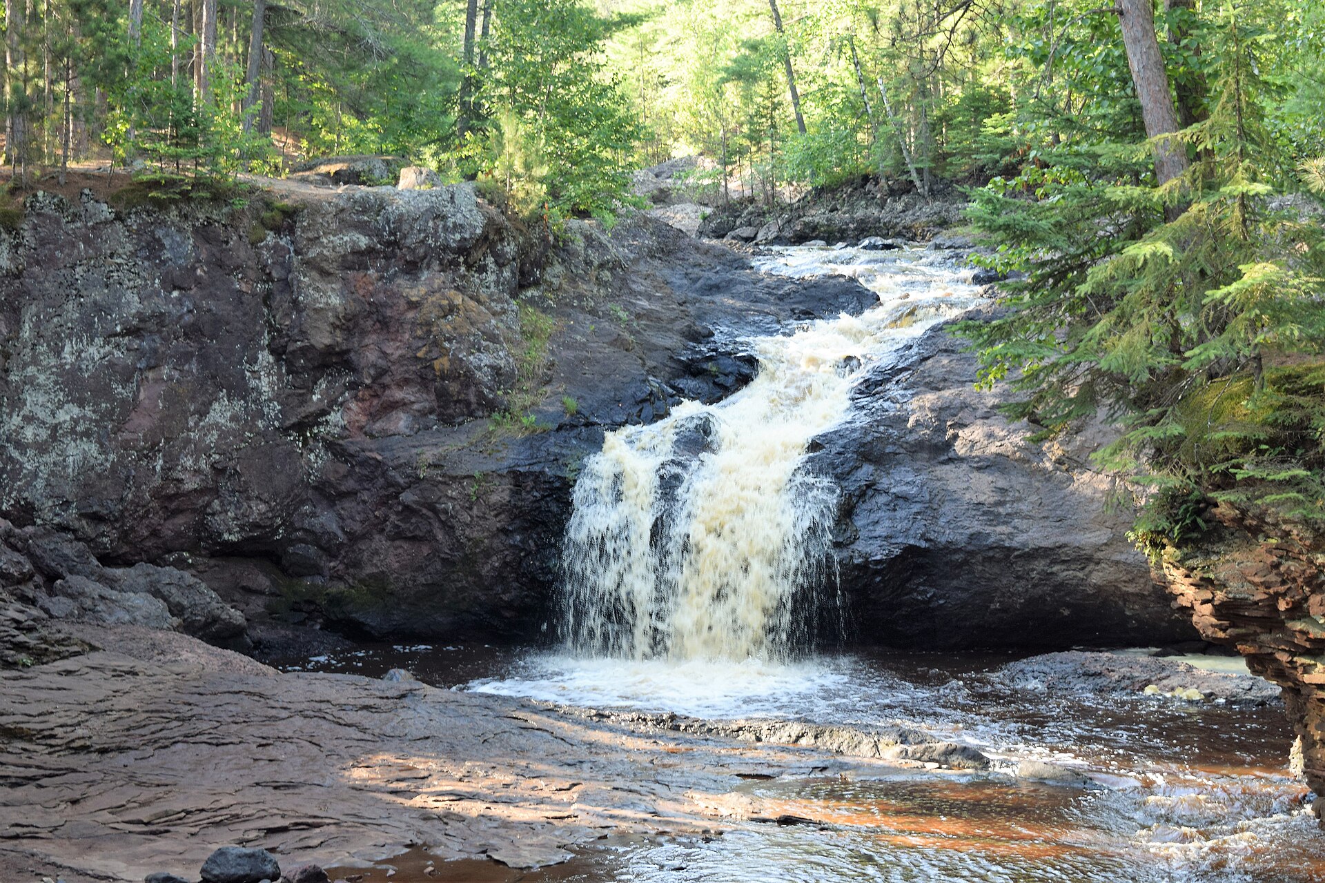 The Amnicon River dropping over a red sandstone ledge into a pool, surrounded by pine and birch woods