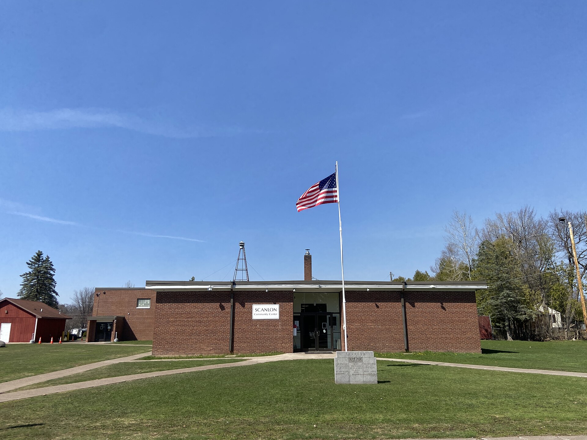 The low brick Scanlon Community Center behind a flagpole and open lawn under a clear sky