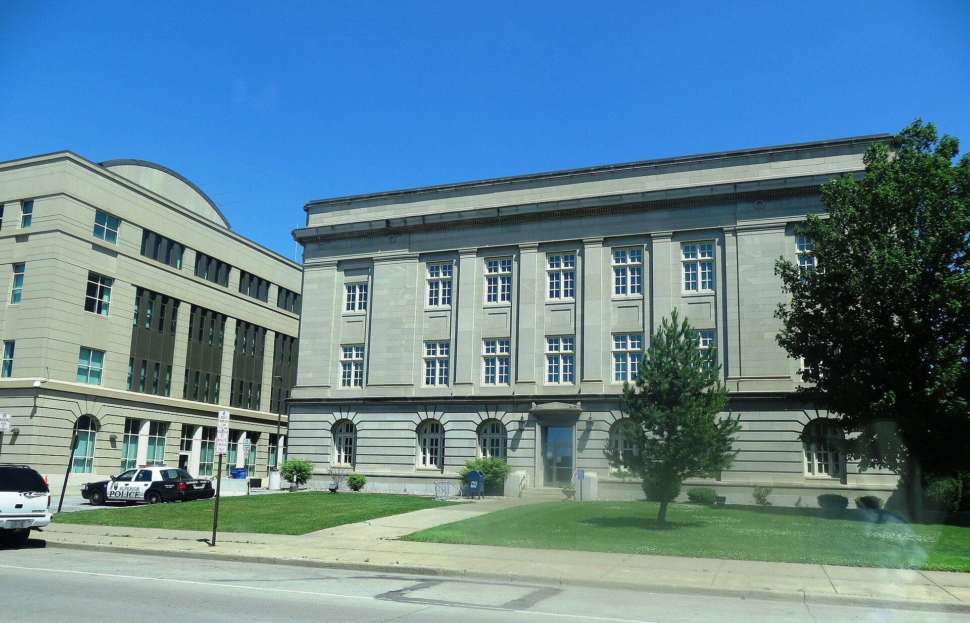 A limestone civic building with tall pilasters on a wide quiet street in Superior, Wisconsin, under a clear summer sky