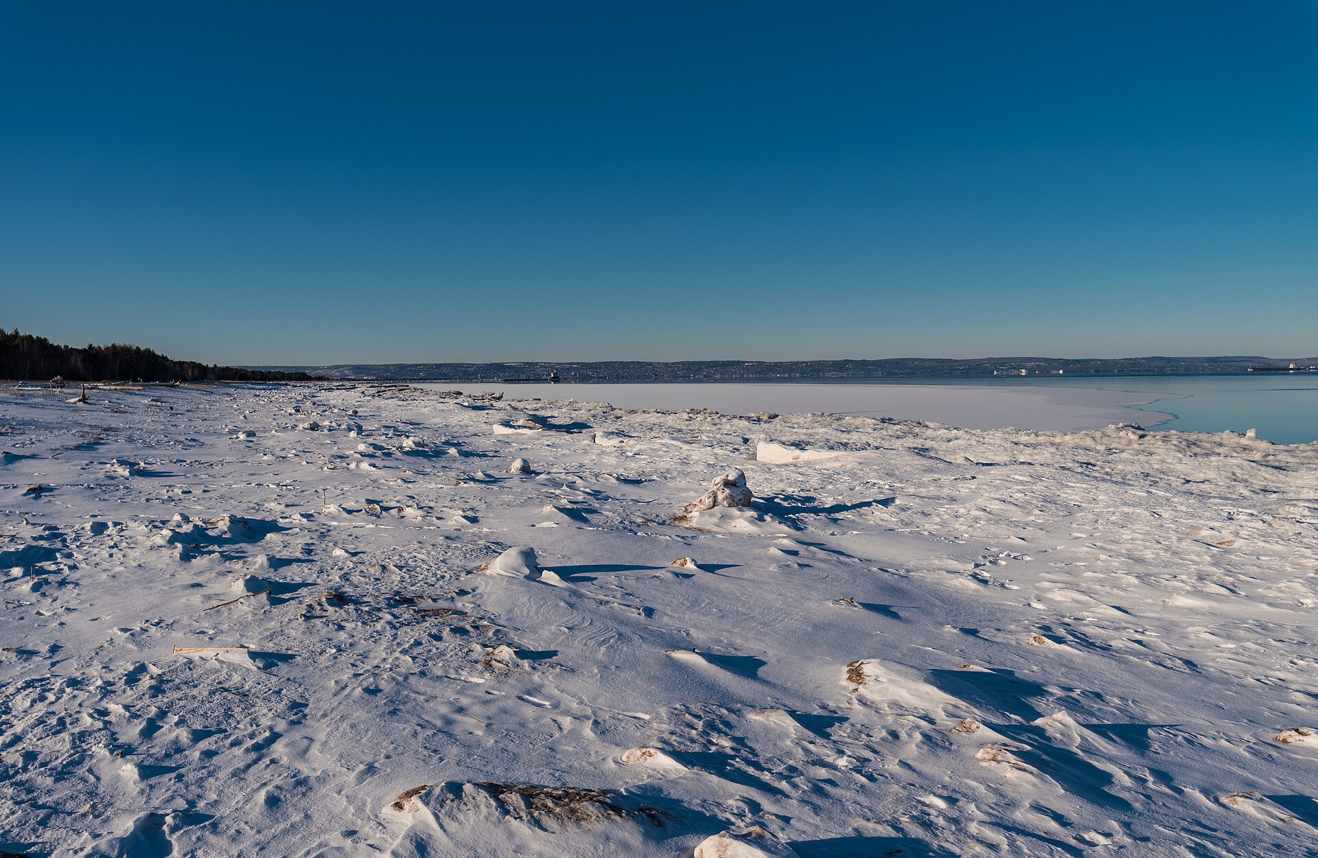 Wind-scoured snow and ice covering a flat beach on Lake Superior at Wisconsin Point under a deep blue winter sky