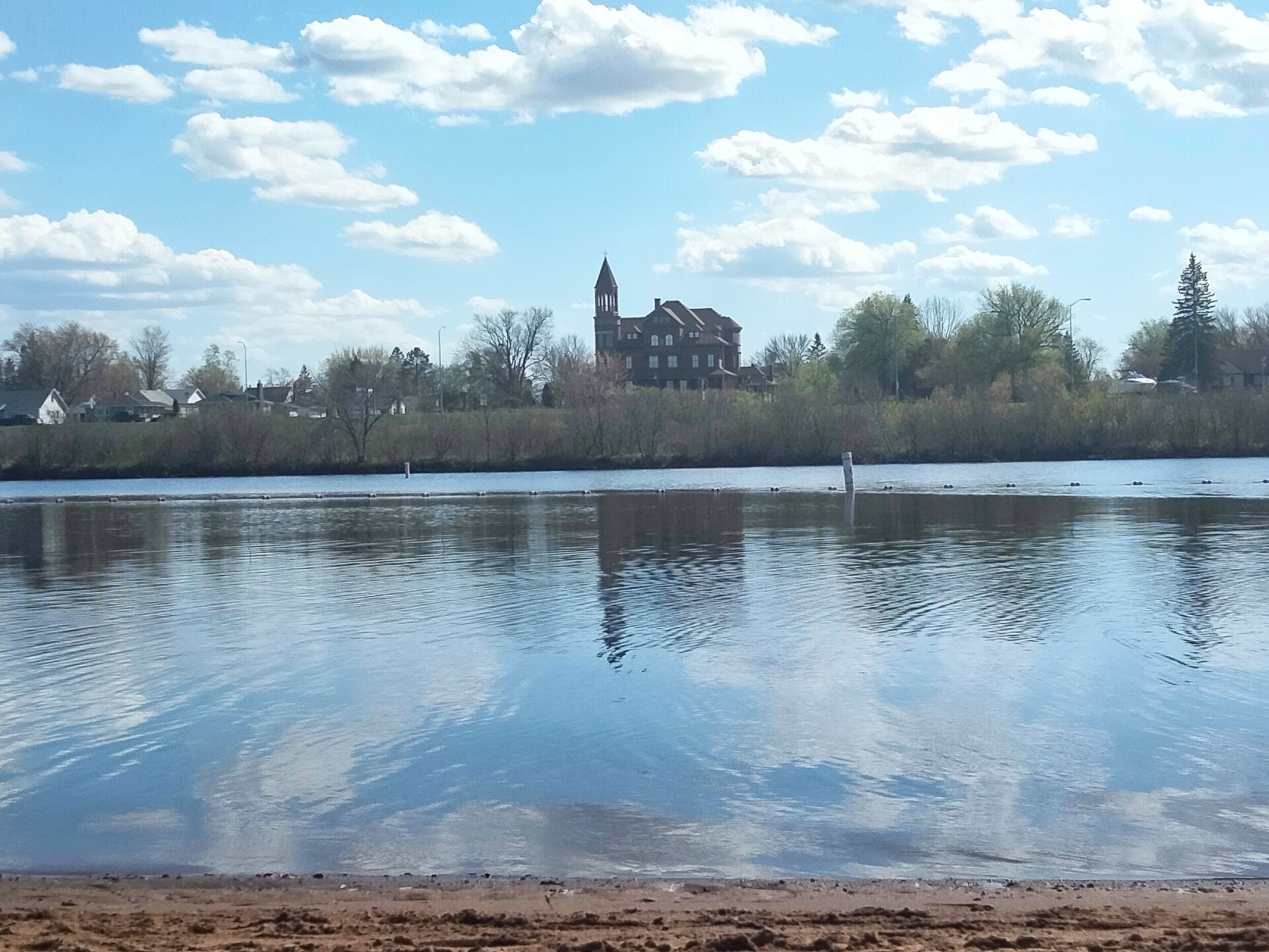 The sand beach and calm water at Barkers Island in Superior, Wisconsin, with the tower of Fairlawn Mansion rising above the far shore