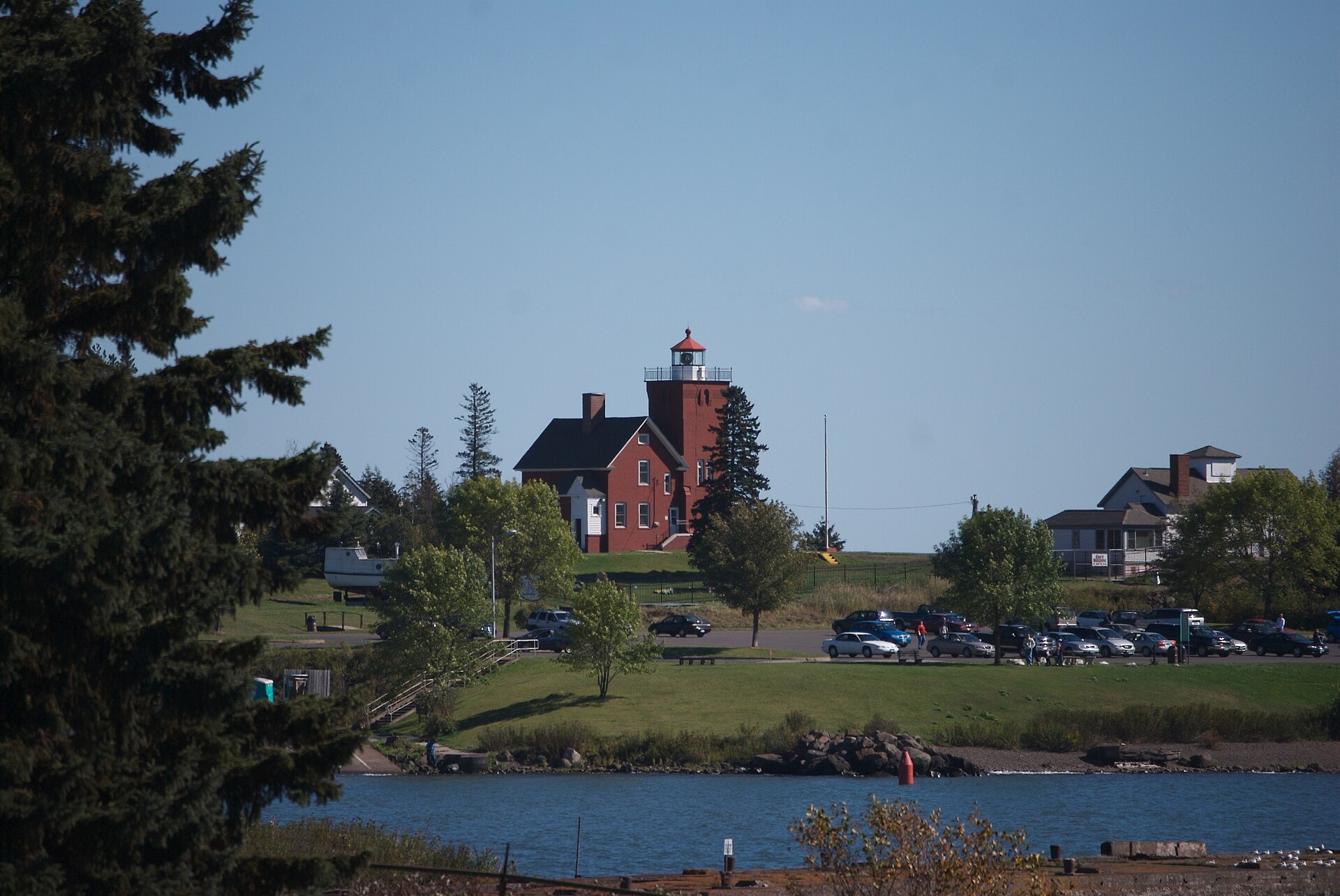 The red brick Two Harbors light station on a grassy point above the water, seen from across the bay